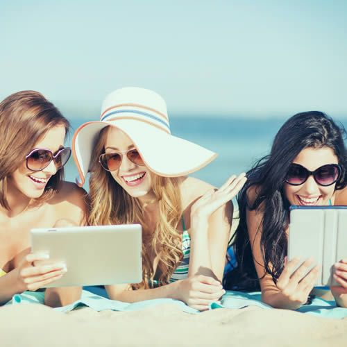 Trois femmes bronzent sur la plage avec leurs tablettes
